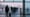 Travelers waiting in cold winter light at a European transport hub with grounded aircraft blurred in fog, no text or logos visible.
